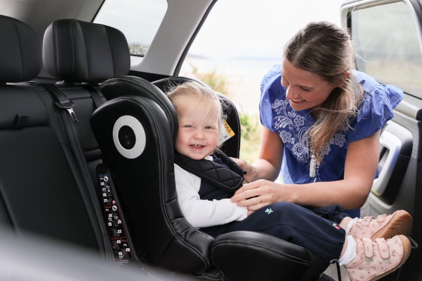Child in car seat with mother helping to buckle seat belt