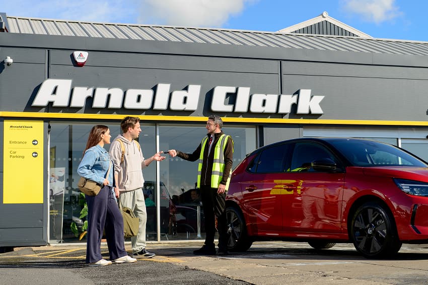 Arnold Clark Rental employee handing over car key to young couple outside branch