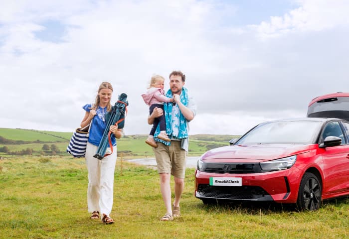 Family by seaside next to red Vauxhall Corsa-E