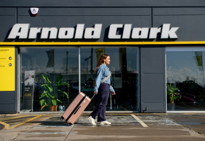 Arnold Clark Rental customer walking with suitcase outside branch